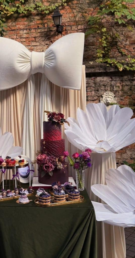 Elegant outdoor dessert table at wedding celebration with flowers, cake, and sweets.