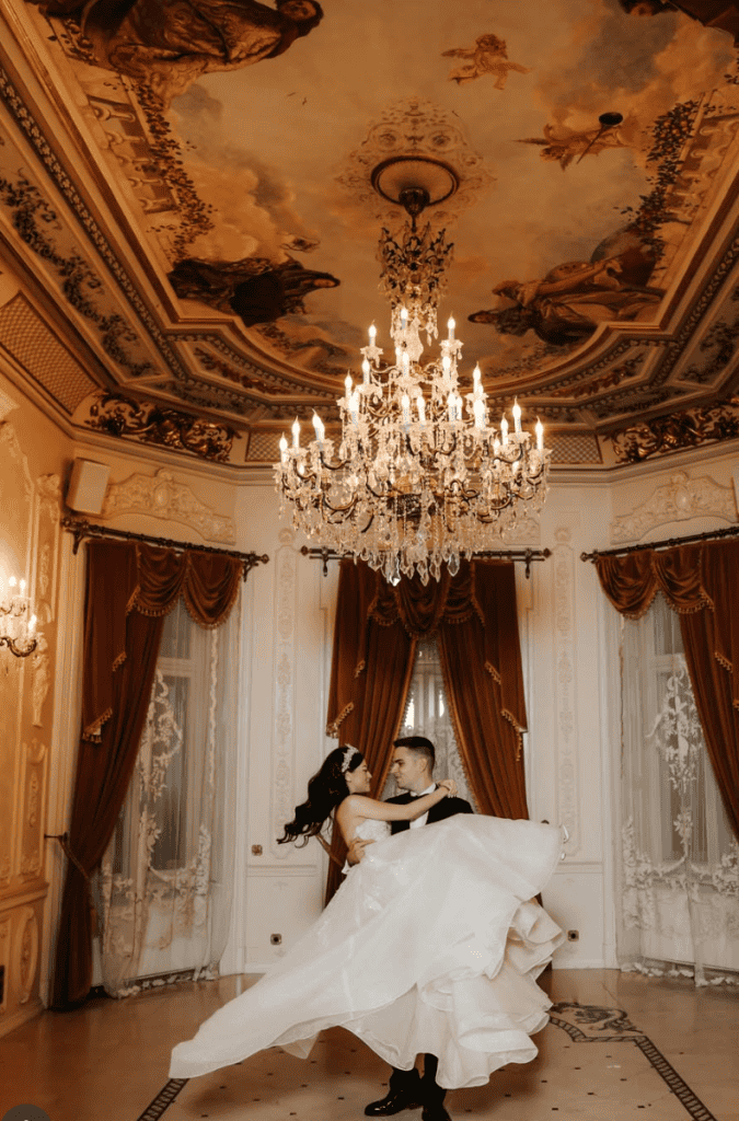 Elegant ballroom wedding dance scene with a chandelier and ornate decor, capturing romantic couple moments.