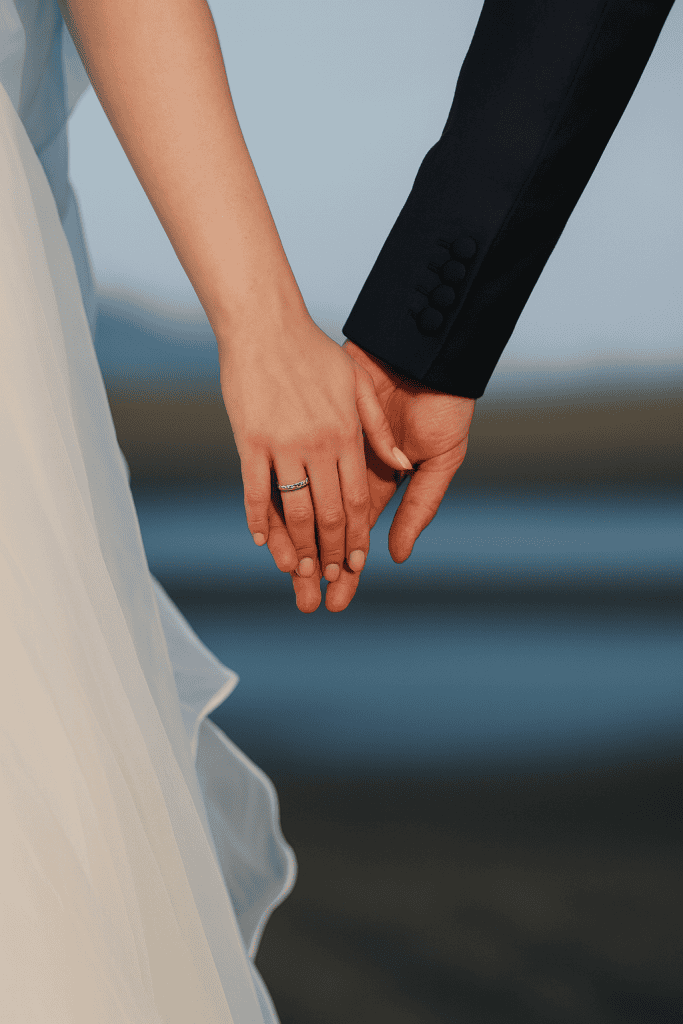 Holding hands of a bride and groom at a wedding, focusing on wedding ring and formal attire.