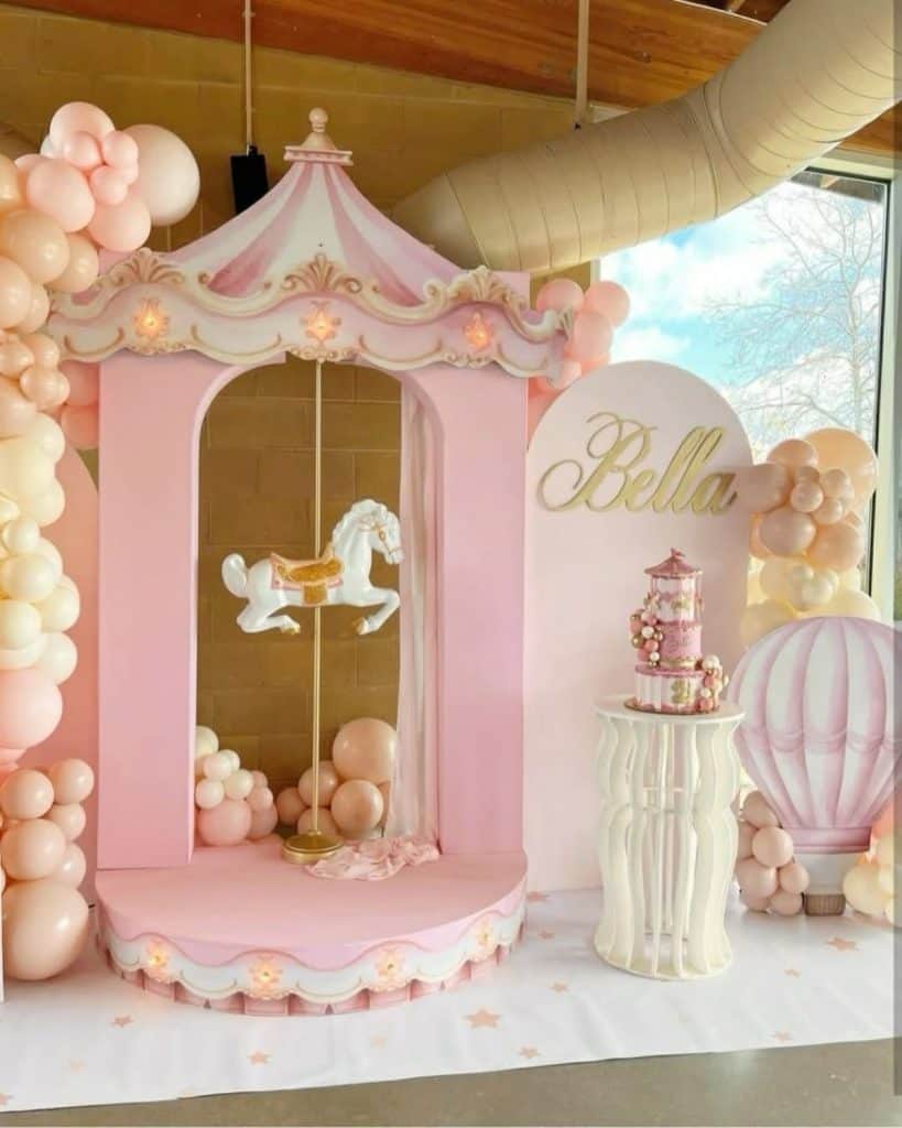 Pink carousel themed birthday party decoration with balloons and cake display.
