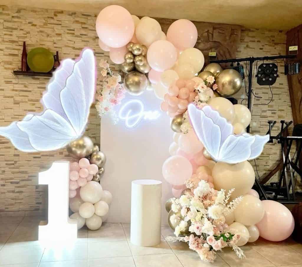 Balloon decoration arch for celebration with pink, white, and gold balloons and butterfly props.