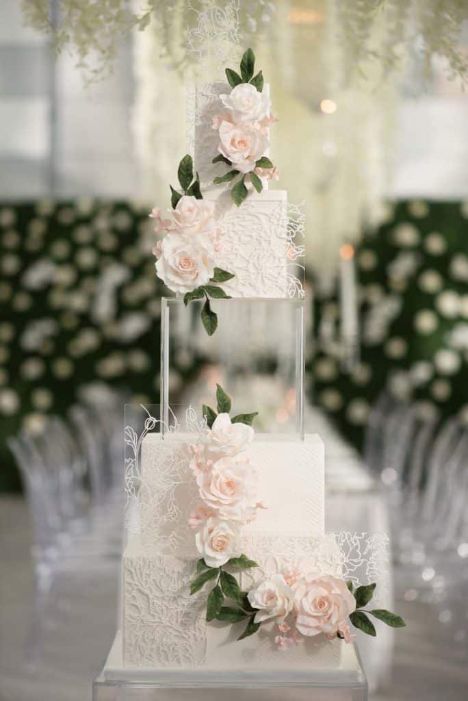 Elegant wedding cake decorated with pink roses and greenery, suitable for upscale events.
