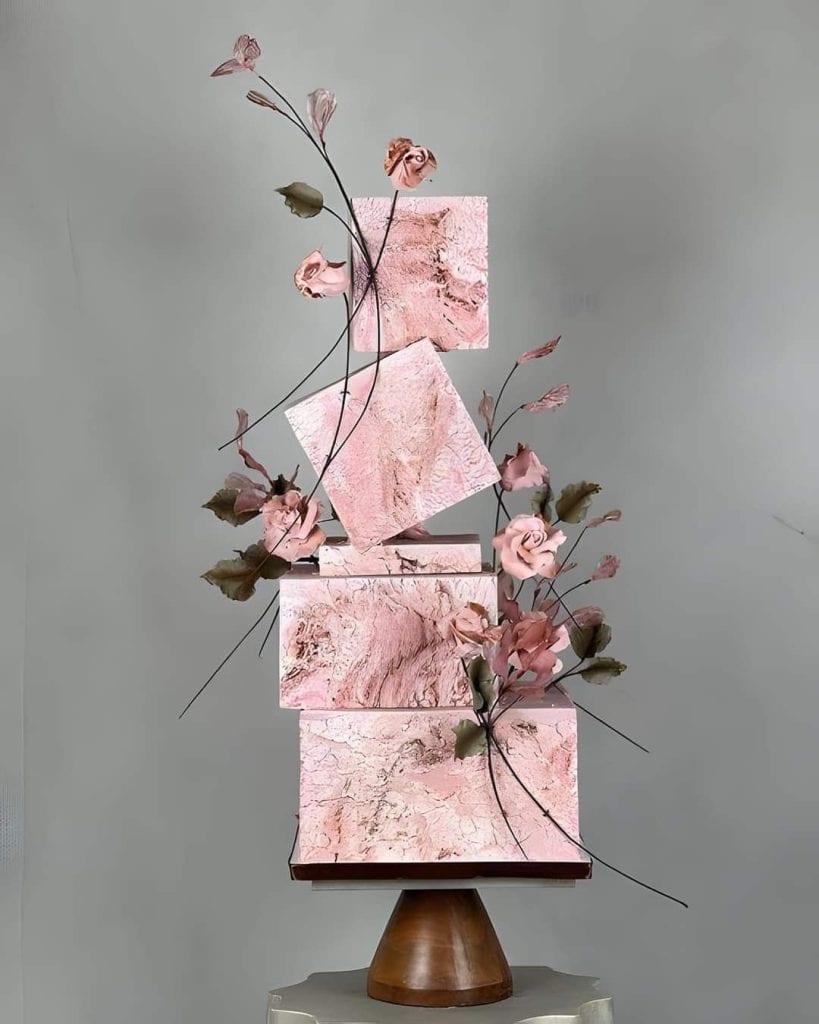 Pink marble geometric sculptures with delicate pink flowers, modern art display for event decoration.