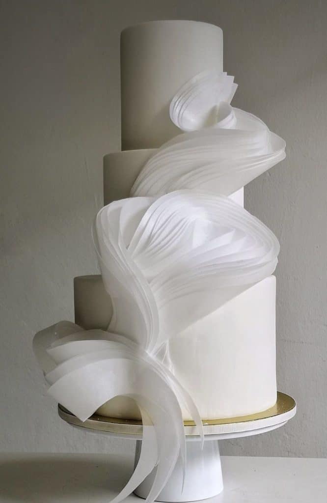 Elegant white wedding cake with modern design and flowing fondant accents.