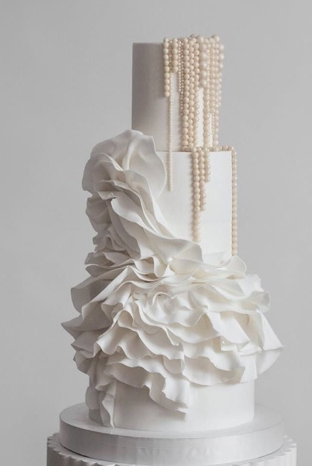 Elegant white wedding cake with ruffled design and pearl accents, perfect for wedding celebrations.