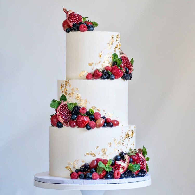 Delicious multi-tiered wedding cake decorated with fresh berries and gold leaf accents.