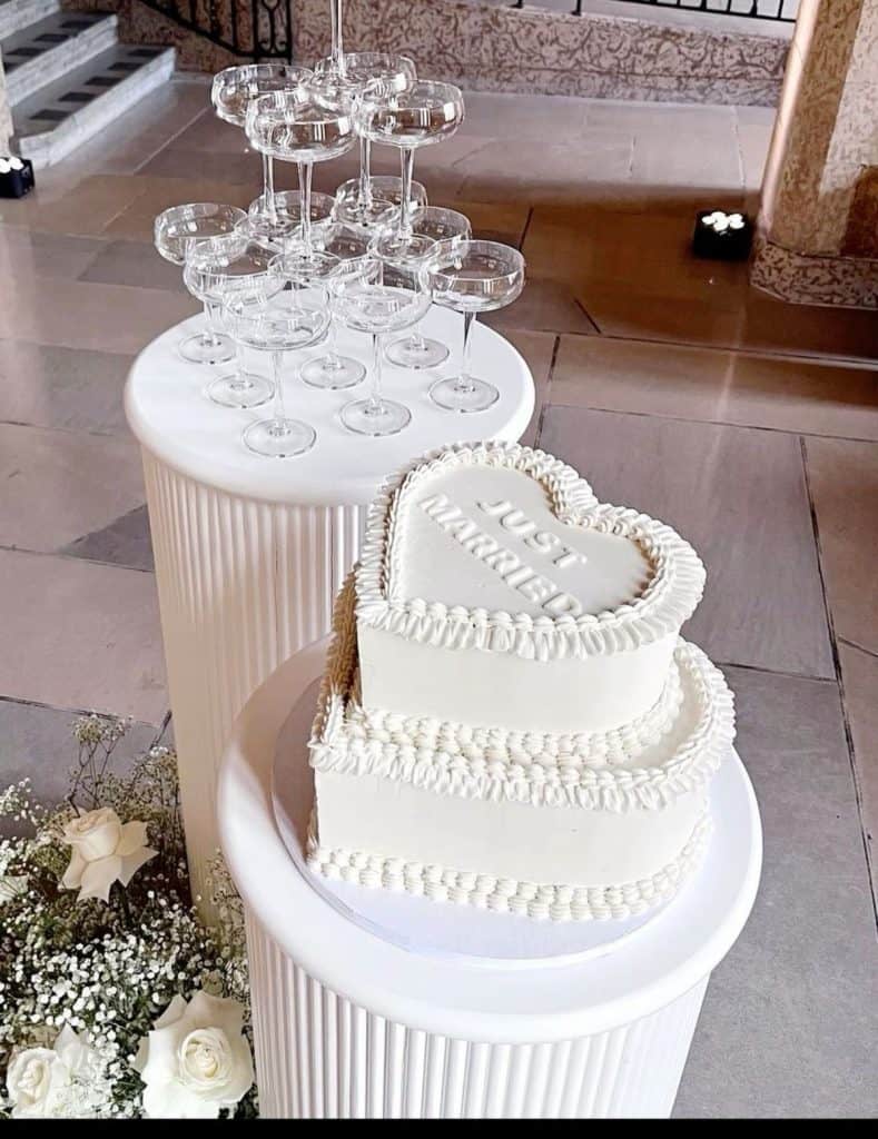 Elegant wedding celebration setup with champagne glasses and a heart-shaped cake on a white pedestal.