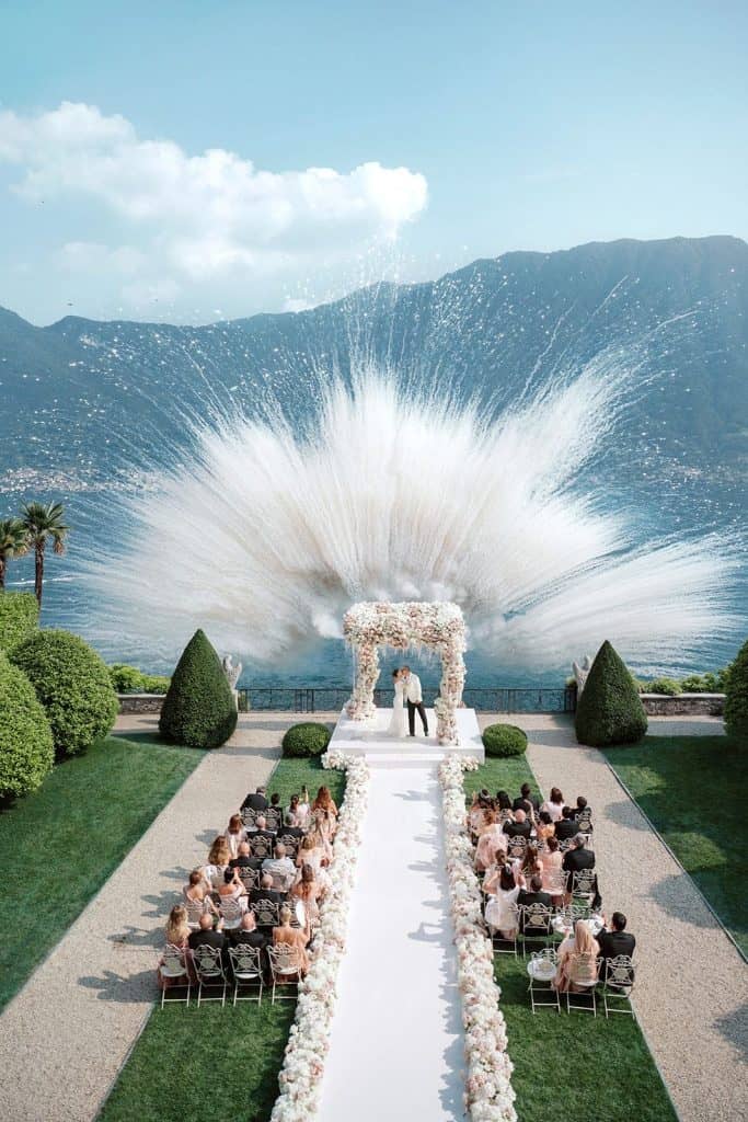 Vows wedding ceremony on a scenic lakeside with mountains, floral arch, and guests seated outdoors.