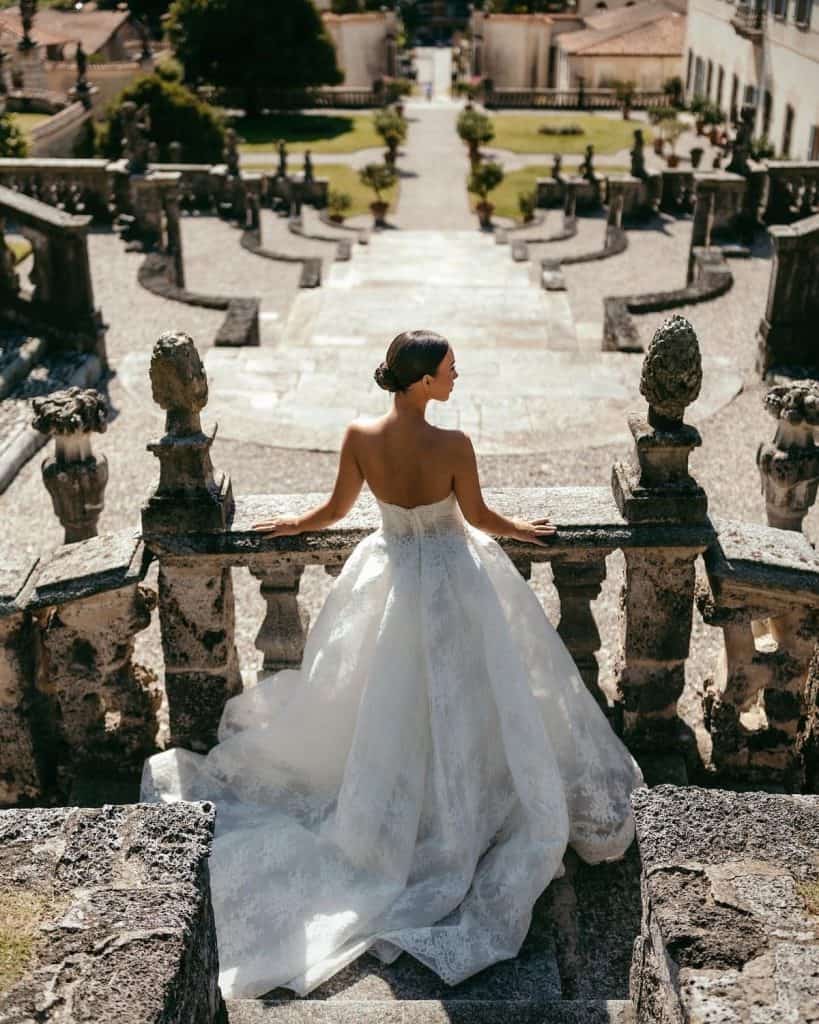 Elegant bride in a white wedding gown on historic stone staircase.