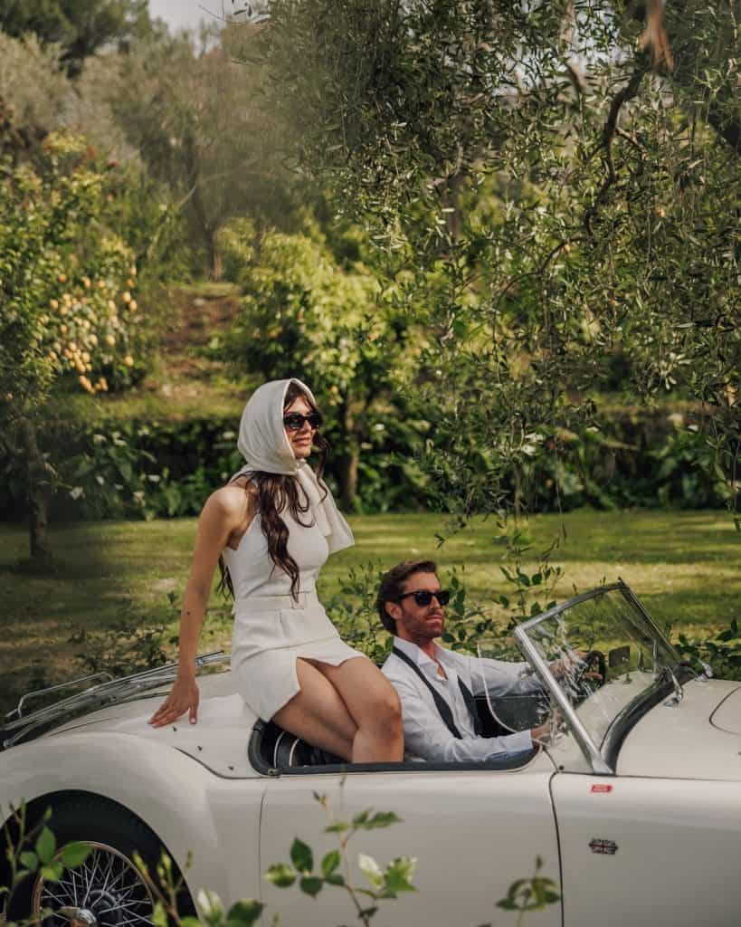 Luxurious vintage car with a woman and man enjoying a sunny outdoor event.