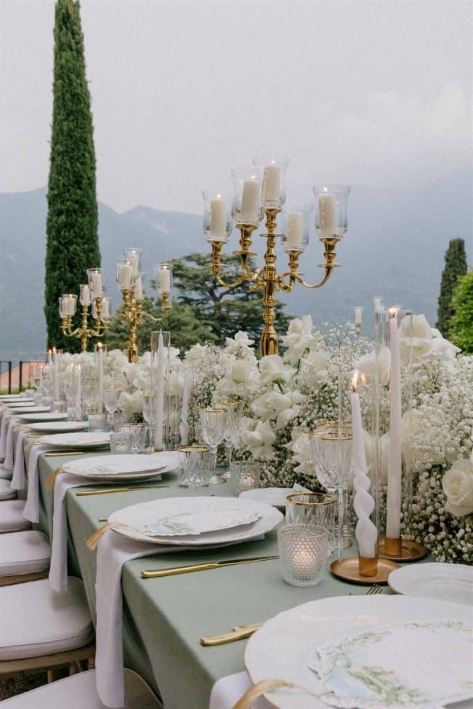Elegant outdoor wedding reception table with gold candelabras and white floral centerpieces for upscale events.