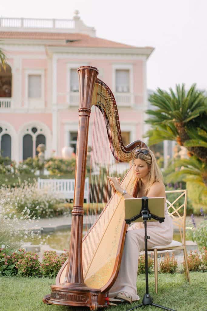 Elegant woman playing harp outdoors at event venue in the garden.