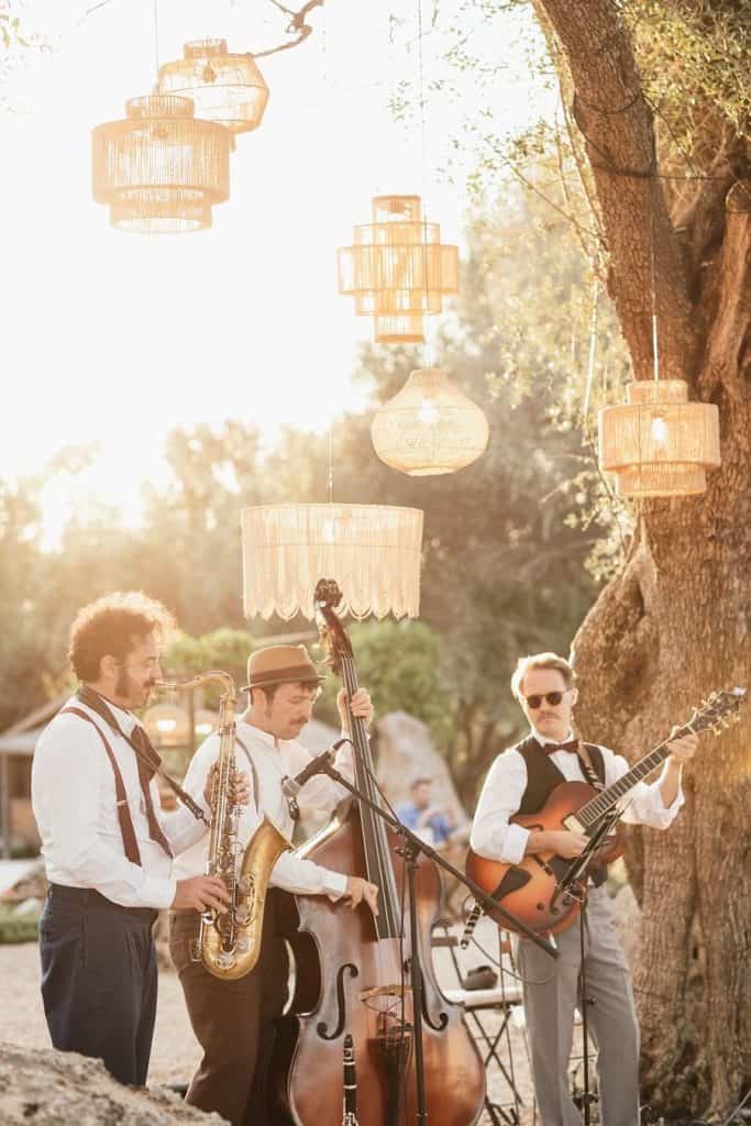 Elegant outdoor jazz band performing at sunset with hanging lanterns, creating a relaxed ambiance for weddings or events.
