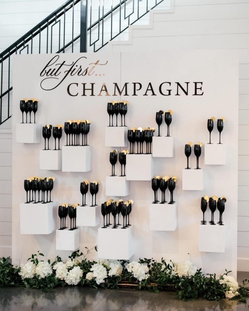 Black champagne glasses on white display shelves with floral decor at an upscale event.