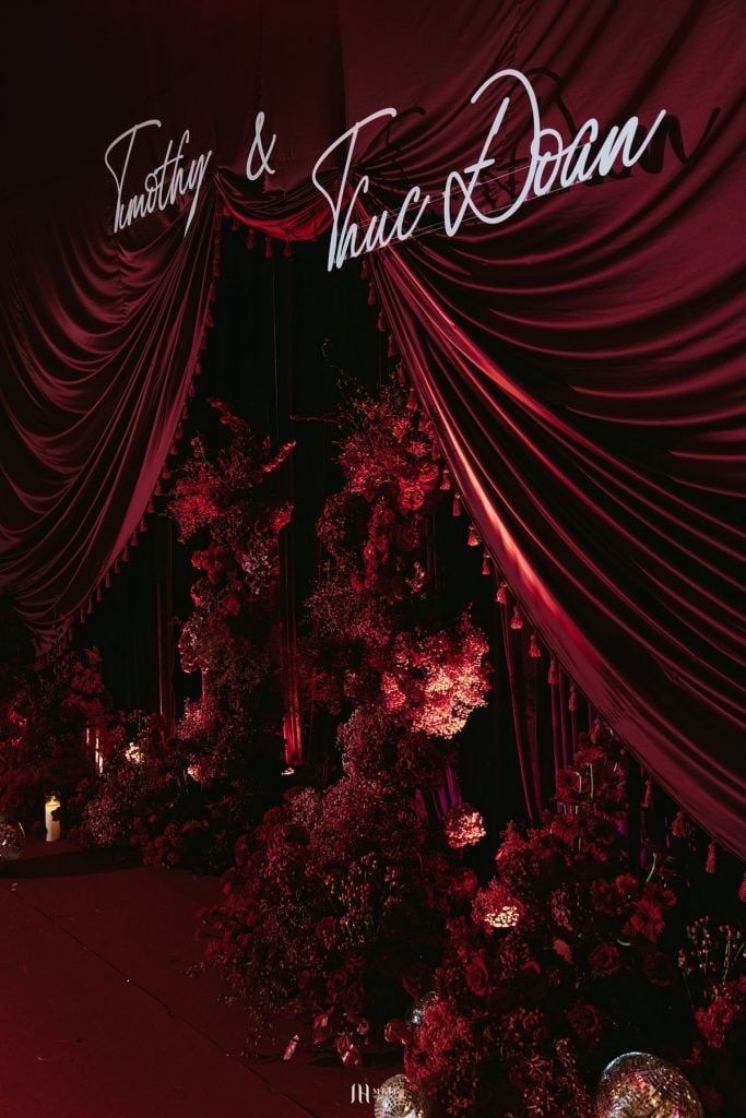 Luxurious event stage with red drapery and floral decorations for upscale celebrations.