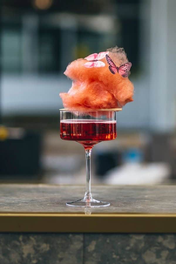 Vape cocktail with cotton candy and butterfly decoration on wine glass.