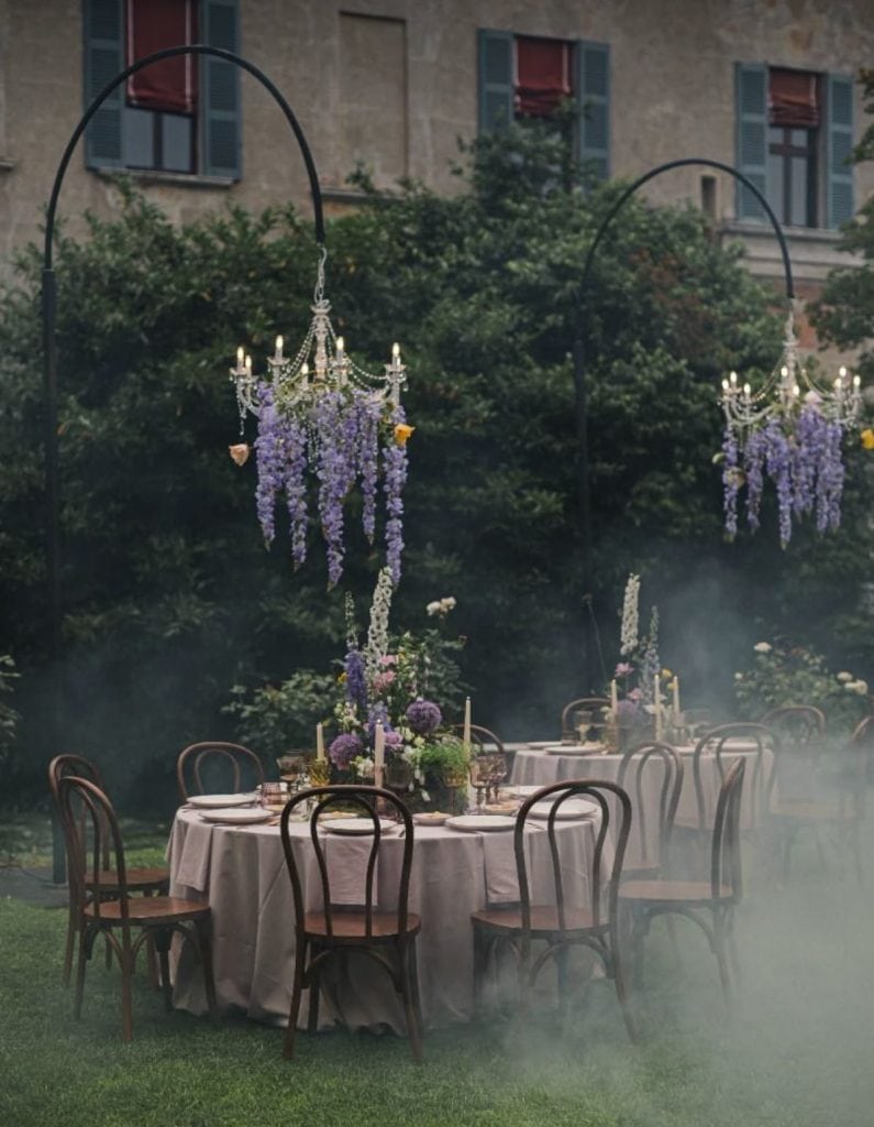 Elegant garden wedding reception setup with chandeliers and floral centerpieces.