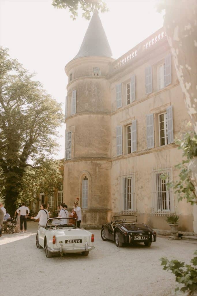 Luxurious vintage cars parked outside a historic castle with a jazz band playing. Elegant event in a picturesque French estate.