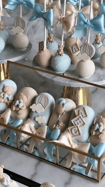 Colorful baby shower cake pops with clouds, balloons, and teddy bear decorations for celebration.