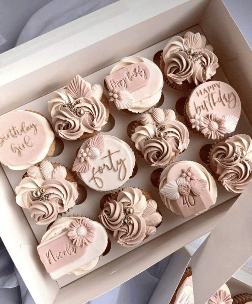 Pink decorated cupcakes with birthday and pregnancy themes, perfect for celebrations.