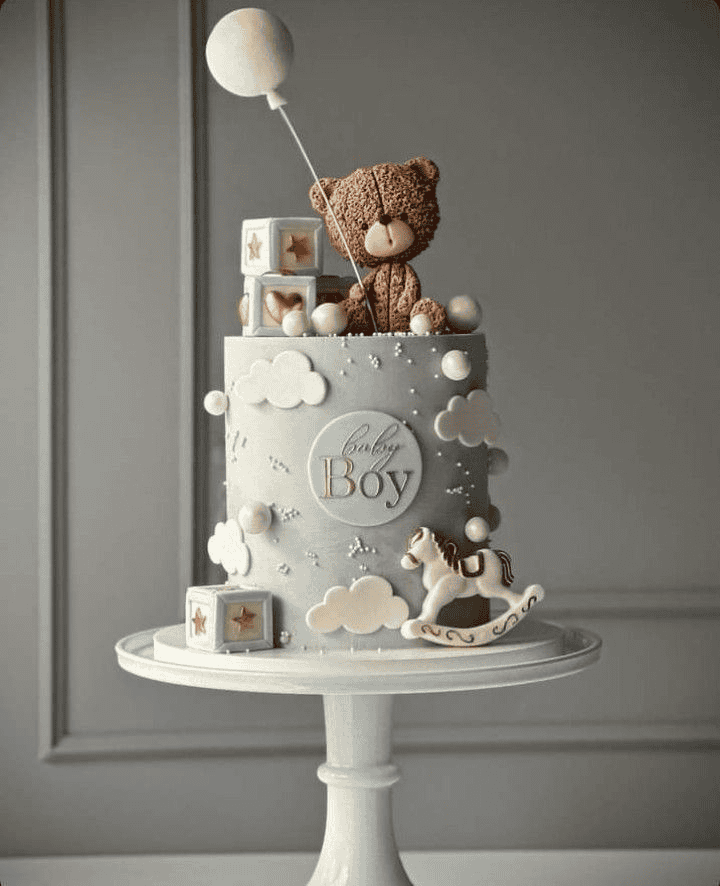 Soft pastel birthday cake with teddy bear and rocking horse decorations for a baby boy celebration.